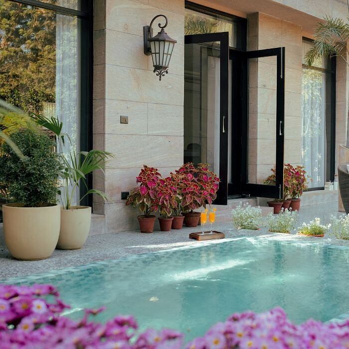 Open glass doors leading to a small pool area surrounded by flower pots and blooming pink flowers at Karma Chalets.