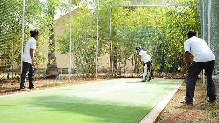 Two people playing a sport on a field, outdoor setting with trees in the background - Shreyas Retreat