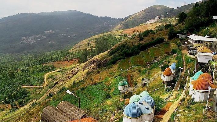 A panoramic shot of a hill station with colourful houses scattered on terraced hills, overlooking misty mountains.