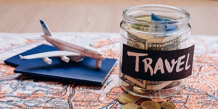 An image featuring a jar labeled Travel, placed next to a plane on a map, with a few coins scattered beside it.