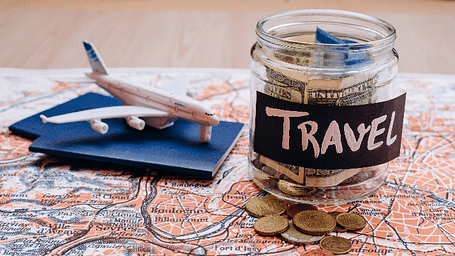 An image featuring a jar labeled Travel, placed next to a plane on a map, with a few coins scattered beside it.
