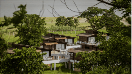 Modern wooden villas on stilts surrounded by lush greenery with a lake visible in the background.