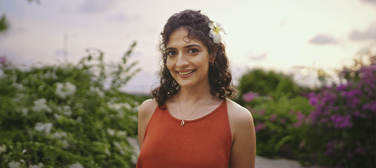 A smiling woman standing outdoors near blooming plants at Athiva Hotels & Resorts.