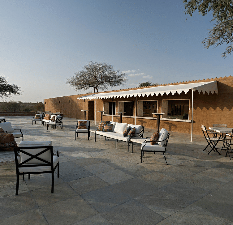 A facade image of the outdoor seating area with chairs and the resort in the background - MANVAR Resort & Desert Camp