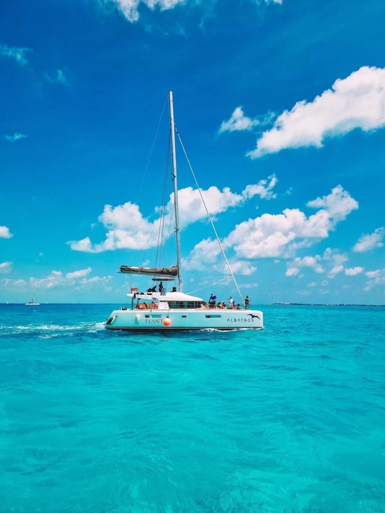 A white catamaran anchored on vivid blue waters under a clear sky with scattered clouds - Tamarind Hills Resort and Villas - Antigua