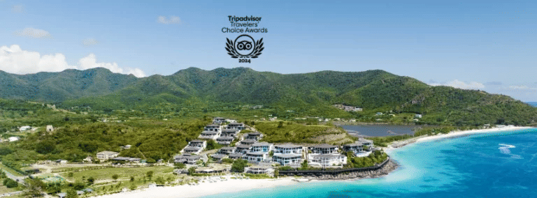 An aerial view of a luxurious resort complex nestled into green hills along a pristine turquoise coast.