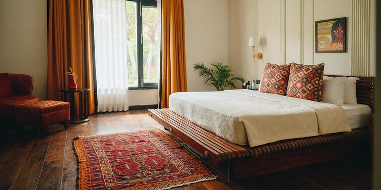 Bedroom with a large bed, armchairs, and a red patterned rug on wooden flooring at Karma Chalets.