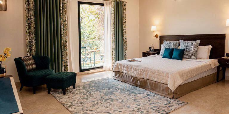 Bedroom with a bed, dark headboard, armchair, and curtains drawn open at Karma Chalets.