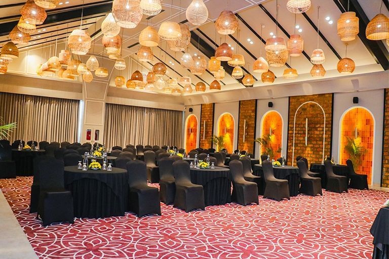 An event hall at Polo Resort Cherrapunjee set up for a banquet with round tables and chairs.