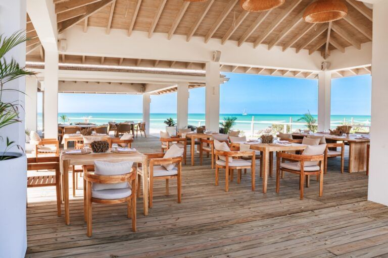 An open-air restaurant with wooden tables and chairs, offering panoramic views of the ocean