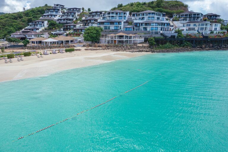 An aerial view of featuring several villas cascading down a hillside to a beautiful white sand beach and turquoise ocean.