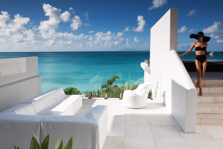 White lounge furniture is set up on a patio with a stunning view of turquoise ocean and a clear sky.