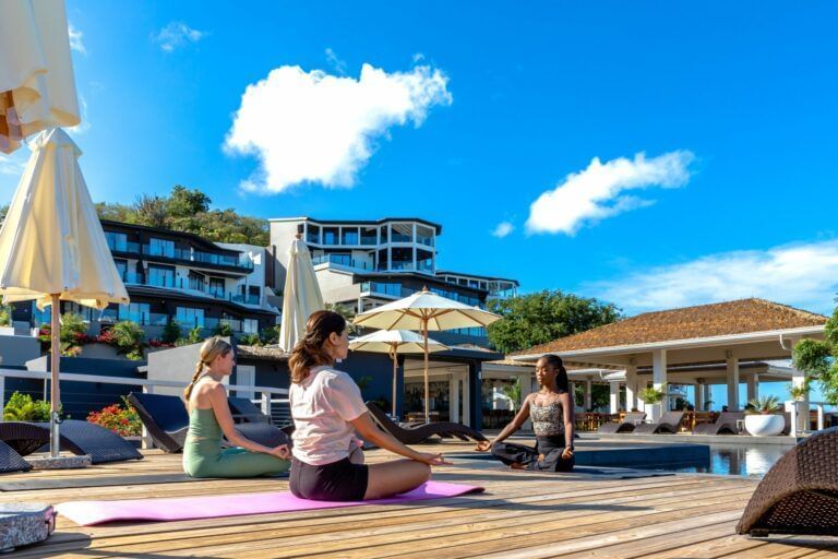People relaxing and participating in an outdoor yoga session or activity near a resort pool area with lush landscaping and ocean views.