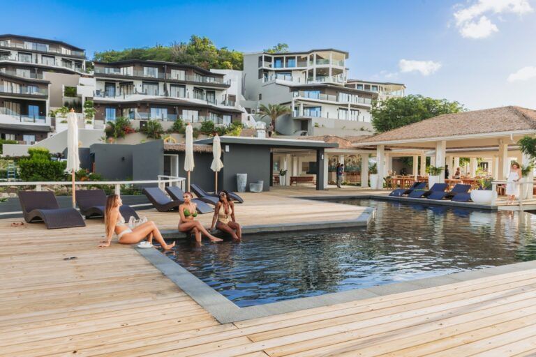 Guests relaxing by a pool with sunbeds at a modern beachfront resort in Antigua.