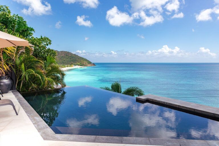 Infinity pool overlooking turquoise Caribbean waters and lush hillside at Tamarind Hills Resorts and Villas, Antigua.