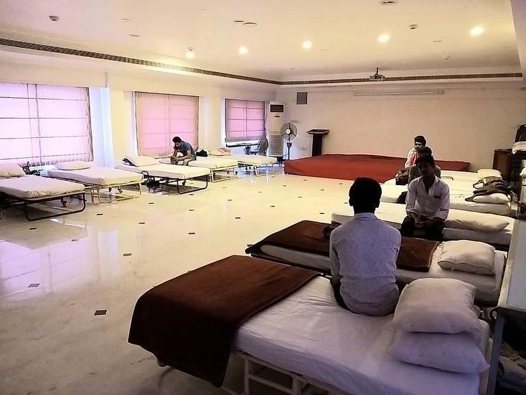 A big hall with rows of beds and people can be seen sitting on them.