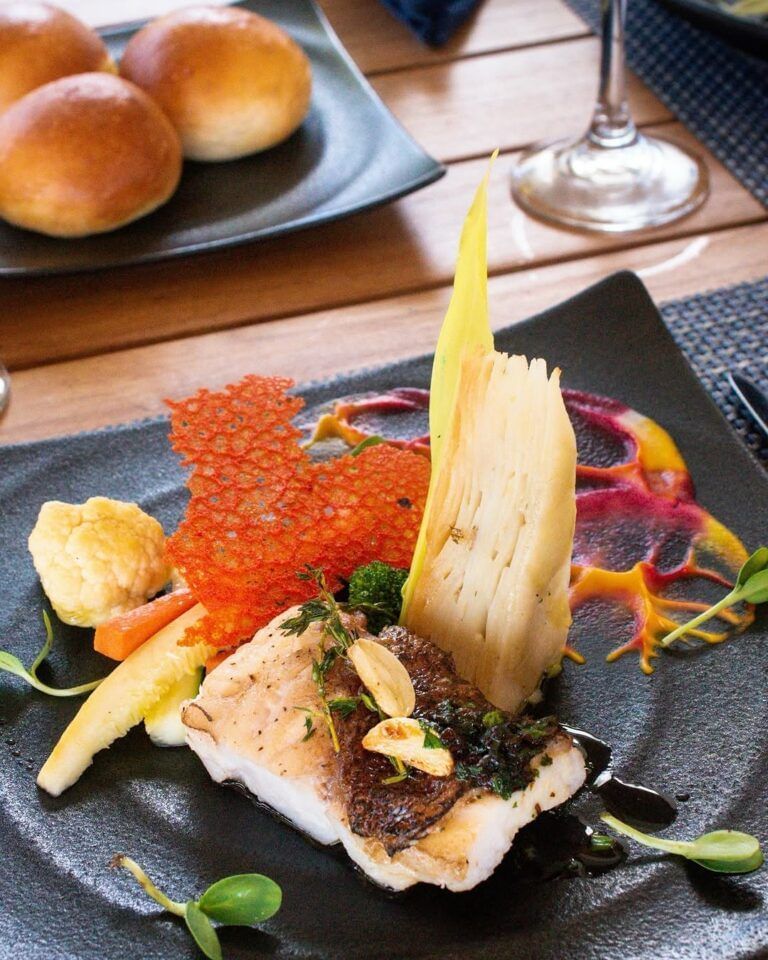 Close-up of a plated gourmet dish with garnish and bread rolls at Tamarind Hills Resort and Villas - Antigua.