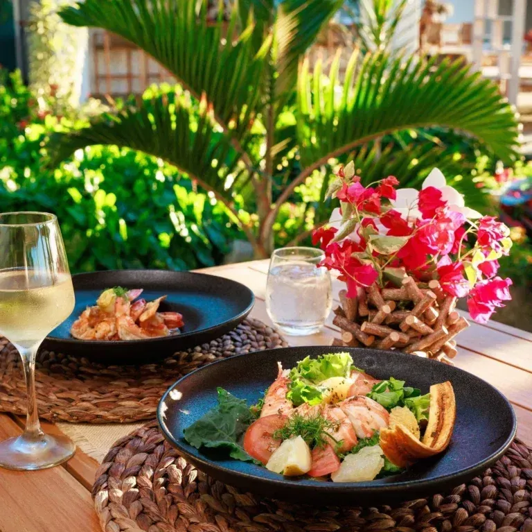 A close-up of two elegantly presented seafood dishes on a table, surrounded by lush green foliage and flowers.
