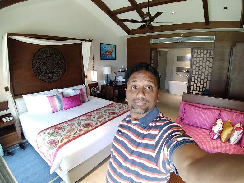 A person taking a selfie in a room in front of the bed.