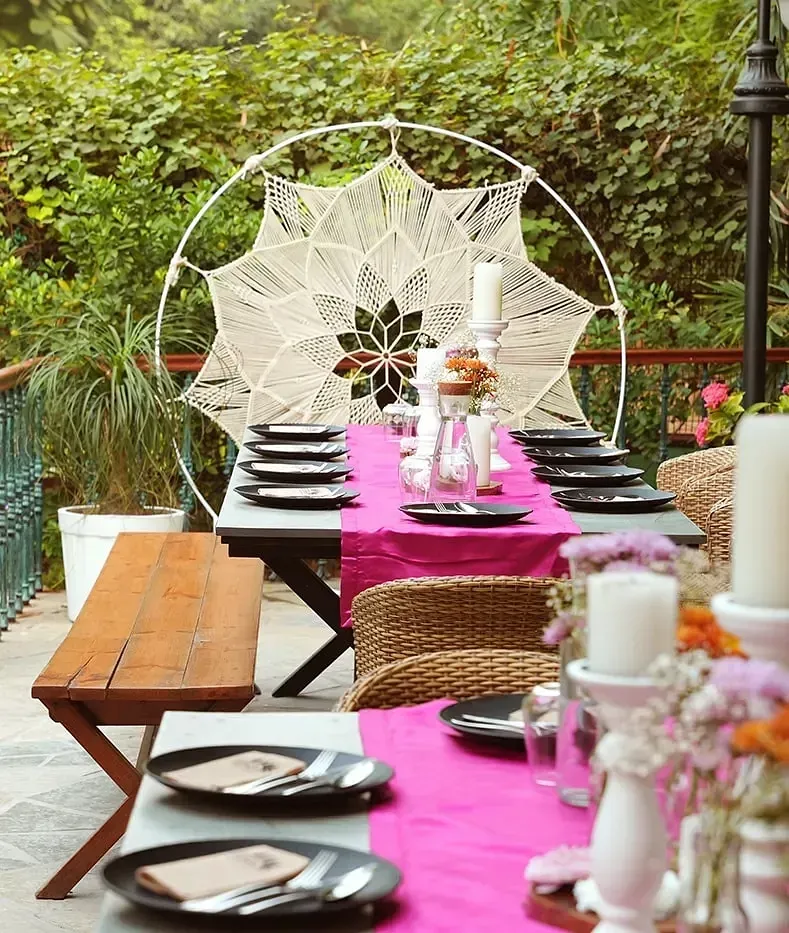 Long outdoor dining table at Karma Chalets with pink tablecloth, white décor, and wooden chairs.