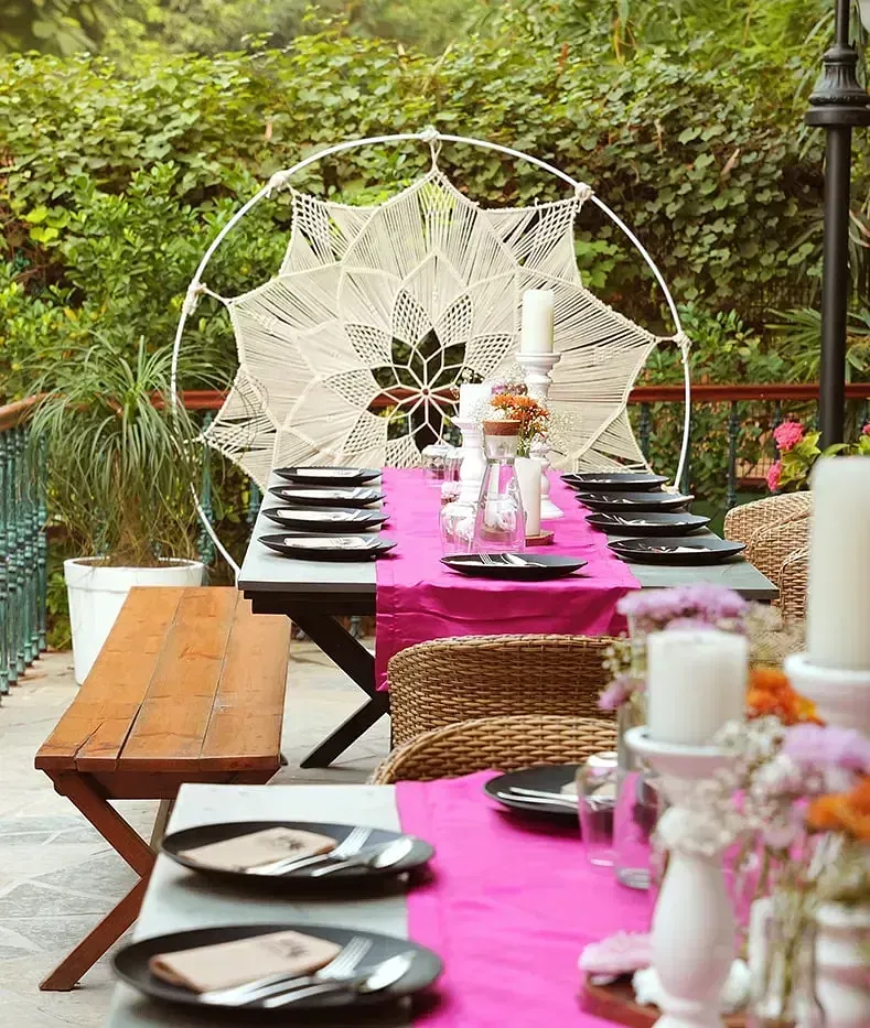 Long outdoor dining table at Karma Chalets with pink tablecloth, white décor, and wooden chairs.