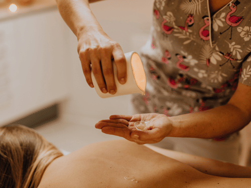 A massage therapist pours warm oil into their hand before applying it to a person lying face down during a relaxation massage.