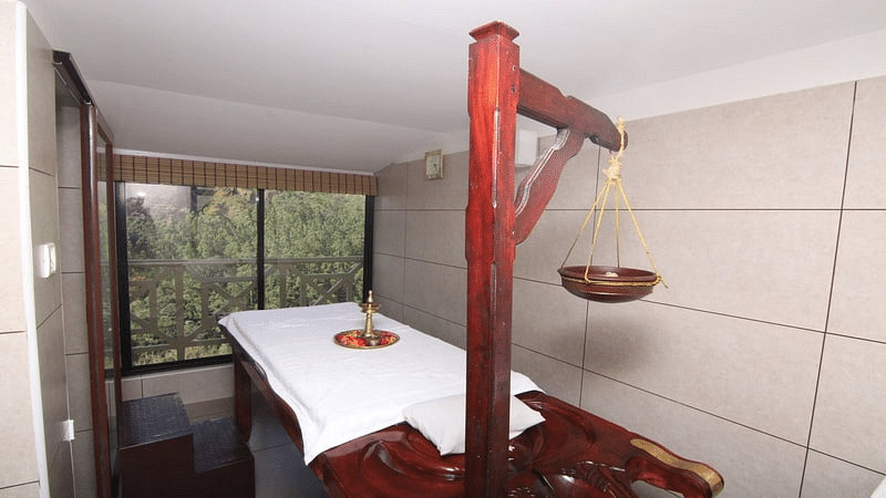 Ayurvedic spa room with a wooden massage table covered in a white sheet - Abad Copper Castle, Munnar