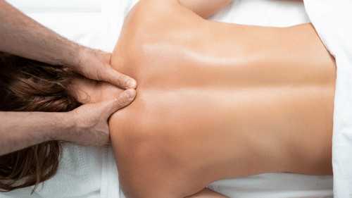 Massage therapist applying pressure to a woman's upper back in a relaxing spa setting, easing tension at YO1 Longevity & Health Resorts