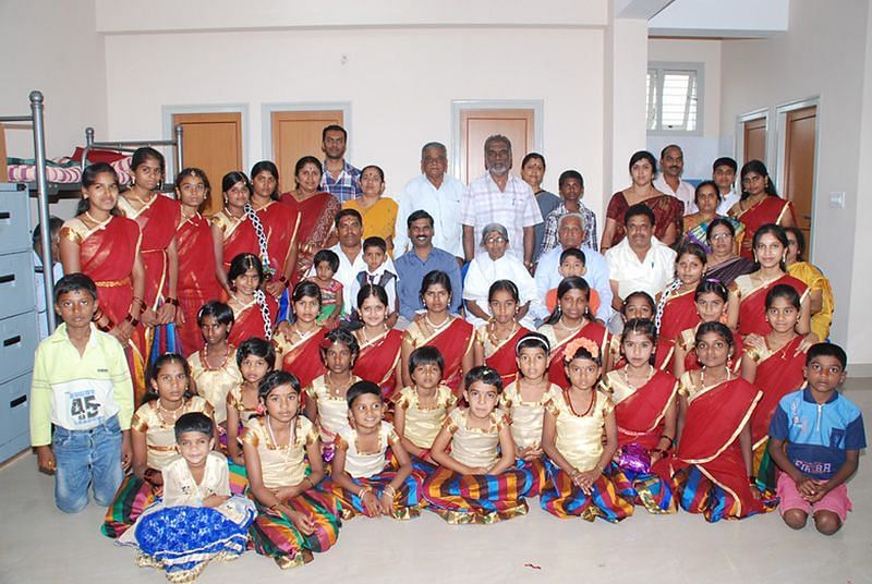 Large group of people, children and adults, posing for a photo indoors, bright clothing - Shreyas Retreat