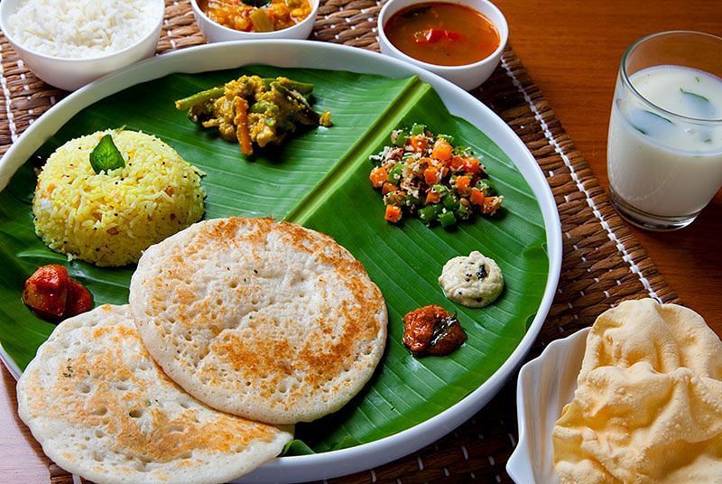 A plate of food with rice, vegetables, and flatbread on a green leaf-shaped plate - Shreyas Retreat
