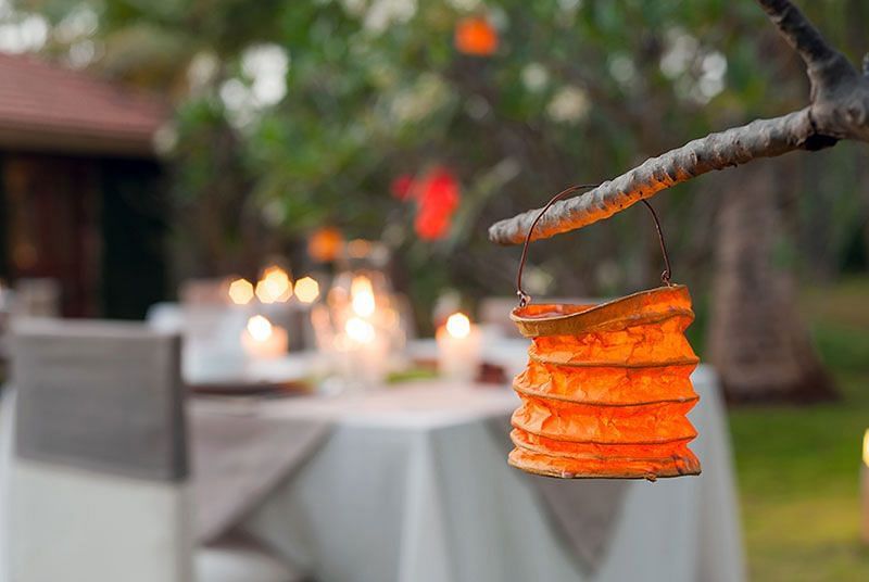 Lantern hanging from a branch over a table with candles, outdoor setting, evening.