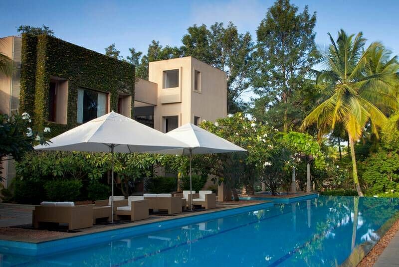 A swimming pool with lounge chairs and a building with a white umbrella, outdoor setting - Shreyas Retreat