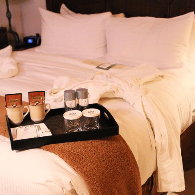 A neatly made hotel bed with crisp white linens and a hospitality tray holding mugs and water bottles.