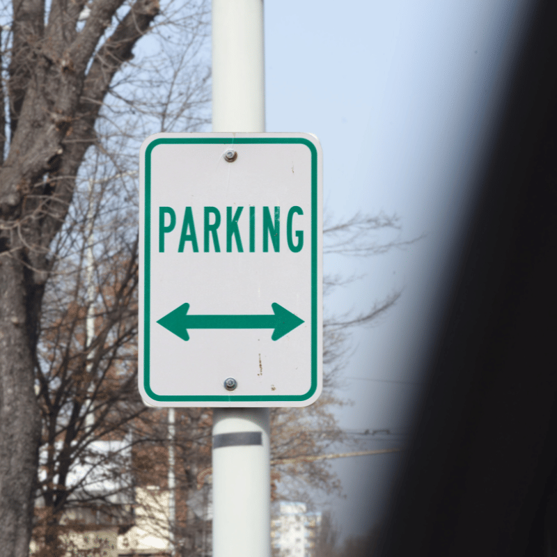 Green and white parking sign with a double-sided arrow mounted on a white pole outdoors.