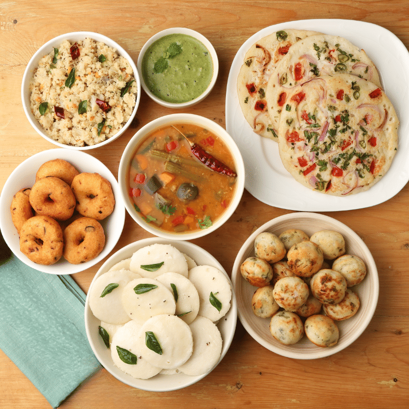 Overhead view of a South Indian breakfast thali featuring idli, vada, uttapam, appe, sambar, and chutney.