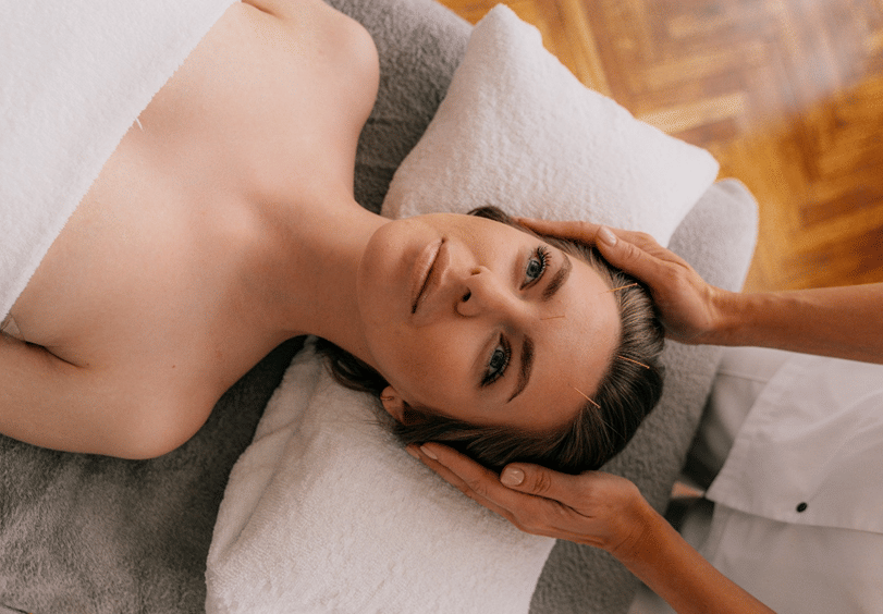Woman lying on a spa bed receiving a gentle head massage, wrapped in a towel, enjoying a calm and soothing wellness experience.
