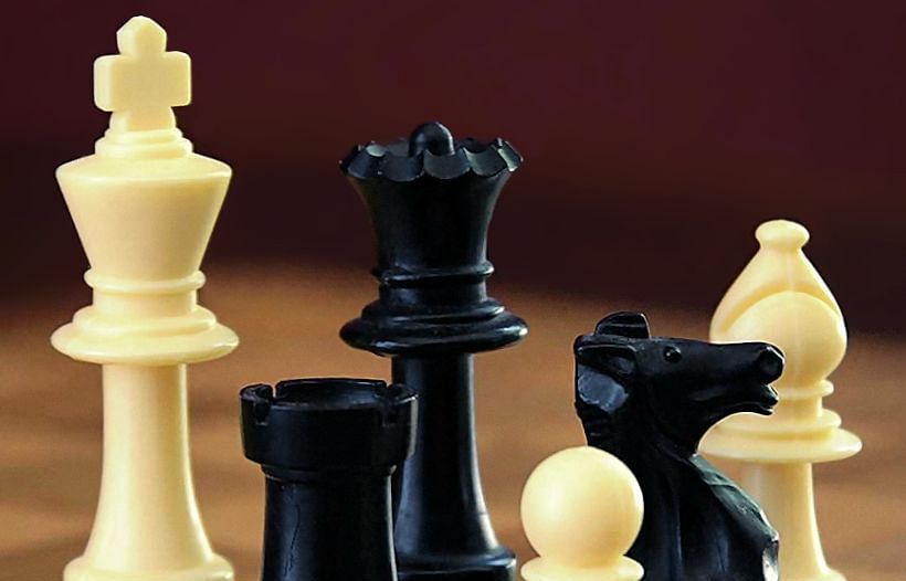 A selection of black and white chess pieces, including kings, a queen and a knight on a wooden surface
