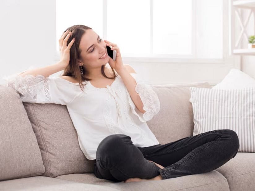 A woman seated on a pink sofa, happily using a mobile phone to talk.