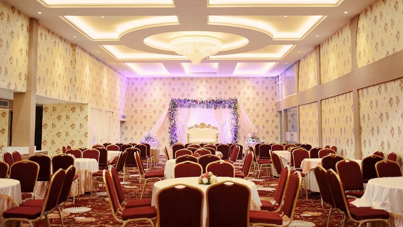 An image of a banquet hall with many table and chairs and at the front there is a stage set up, decorated with flowers and curtains 