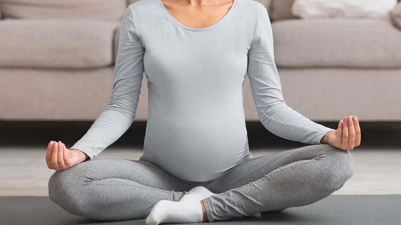 A pregnant woman sitting in a yoga pose, practicing prenatal yoga in a cozy living room.