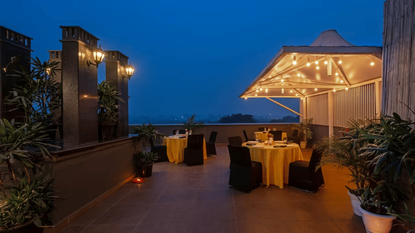 Rooftop dining setup at Hotel Saket 27 with candlelit tables, lush greenery, and a serene evening atmosphere .