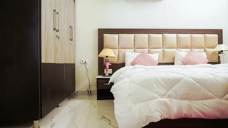 Bedroom of Lime Tree Hotels & Service Apartment Private Limited featuring a tan padded headboard, pink cushions, and bedside lamps.