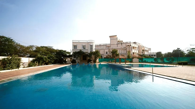 A large outdoor swimming pool with a multi-story building in the background under a clear sky.