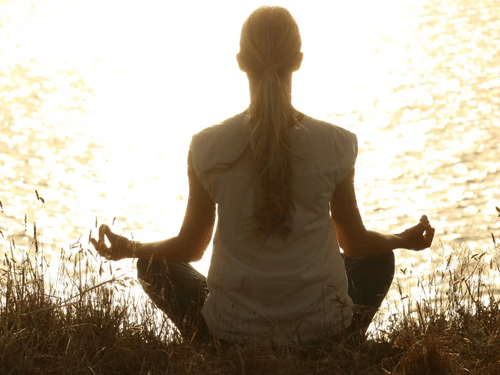  A person sitting in a meditative pose by a lake at sunset, reflecting tranquility and mindfulness.