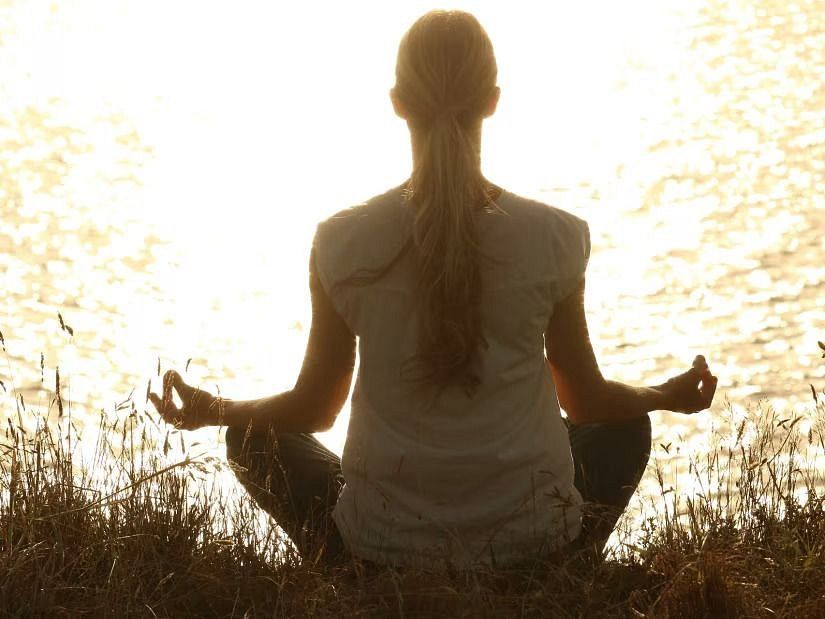  A person sitting in a meditative pose by a lake at sunset, reflecting tranquility and mindfulness.