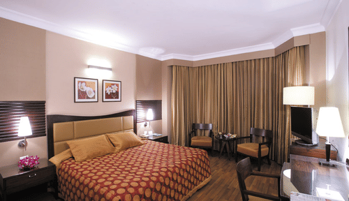 A bedroom of the Executive Room at The Retreat Hotel and Convention Centre, with a king sized bed, a desk, three chair, a bedside table and lamps.