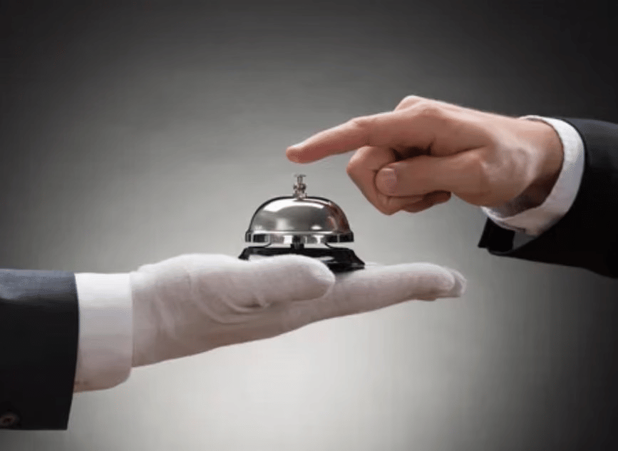 A person wearing a glove holding a service bell while another hand reaches to press it.