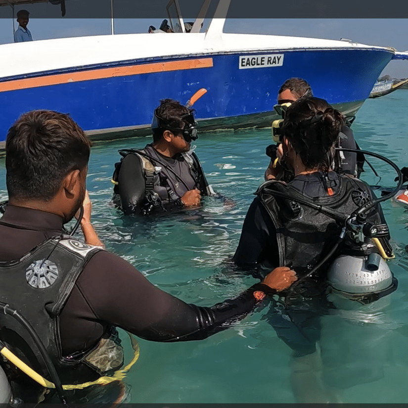 A group of scuba divers in the water receiving instructions and preparing for a dive.