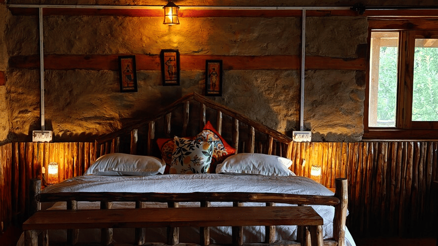 Front-view shot of the double bed at the Hamta Peak Cottage featuring brightly-lit table lamps on either side of the bed along with 3 photo frames hung on the wall behind the headboard of the bed at Amara Upepo - The Sky Village, Manali.