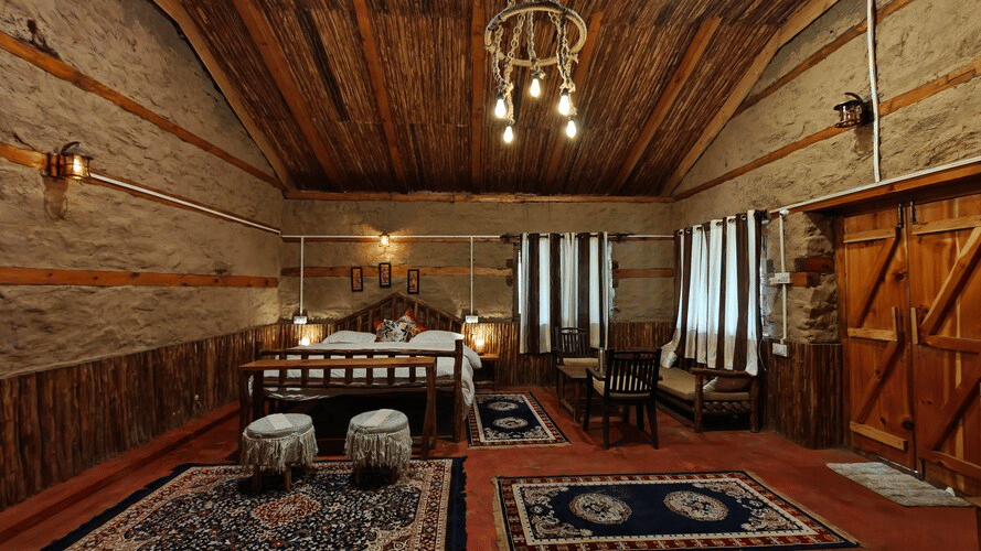 Front view of the entire Hamta Peak Cottage decorated with several pattered rugs placed on the floor, along with a double bed in the corner at Amara Upepo - The Sky Village, Manali.